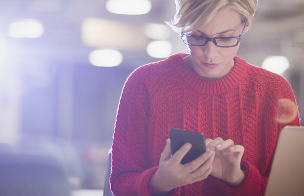 Businesswoman working late at laptop, texting with cell phone in dark office